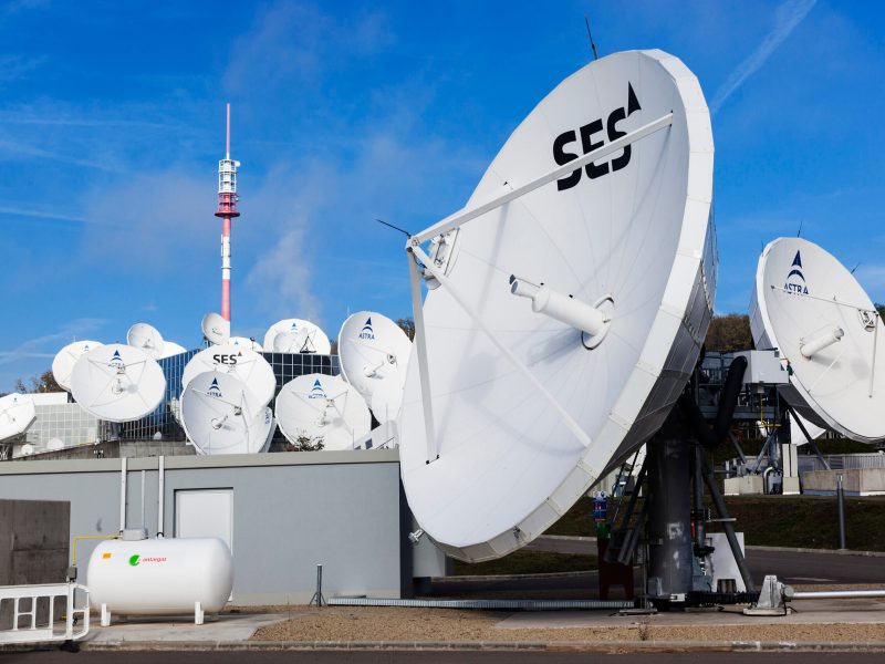 A photo of white satellite dishes against a blue sky. The dish in the foreground is labeled SES.