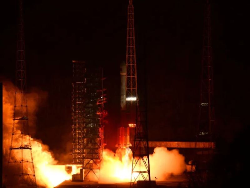Orange exhaust illuminates launch tower infrastructure during nighttime at Xichang spaceport as a Long March 3B rocket carrying the Zhongxing-26 (ChinaSat-26) satellite lifts off.